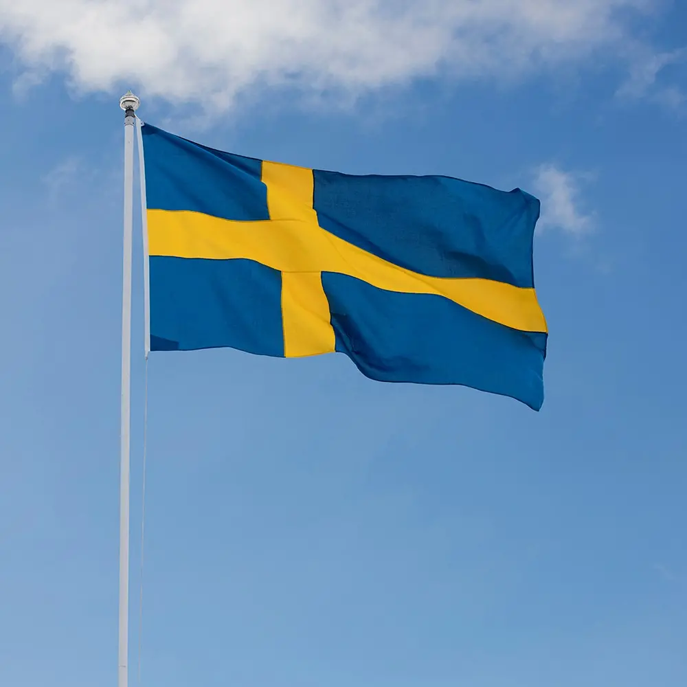 Svenska flaggan vajar på en flaggstång, blå himmel och solsken.