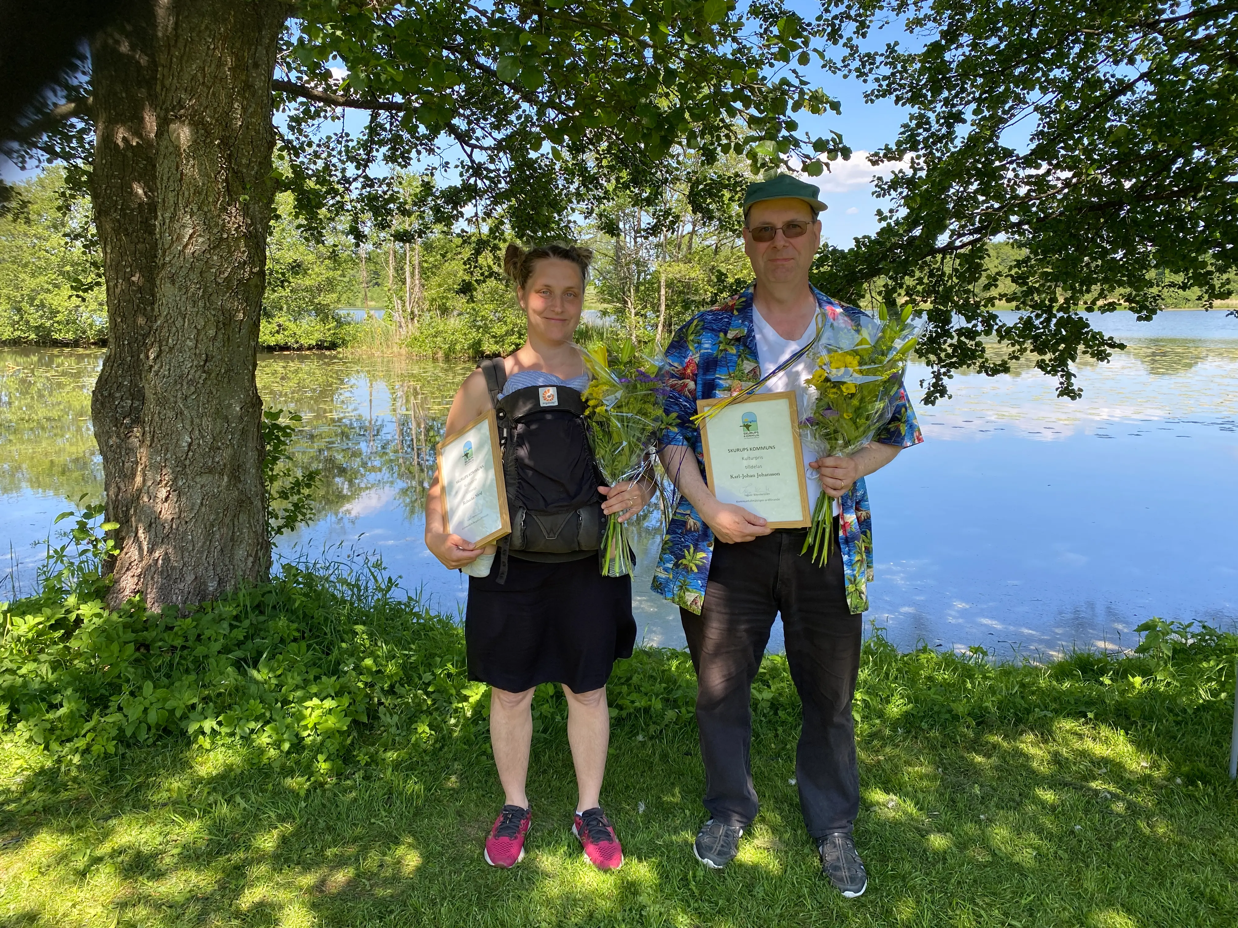 Bild på två personer som mottagit diplom och blombukett. Står framför Svaneholm sjön.