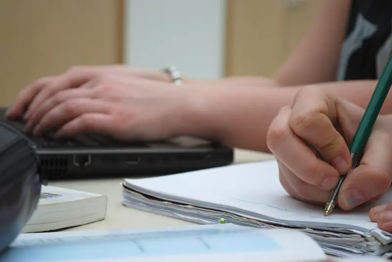 Ett par händer som skriver och använder dator på ett skrivbord.