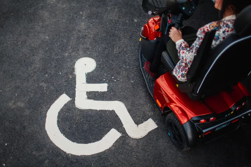 En person med en permobil på en parkeringsplats med symbol för funktionshinder.