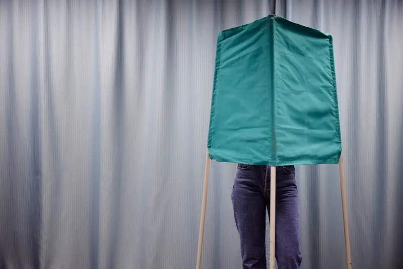 En person står bakom ett grönt valbås.