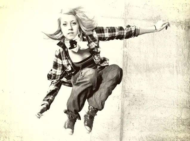Ung person dansar streetdans och hoppar upp i luften, ljus bakgrund.