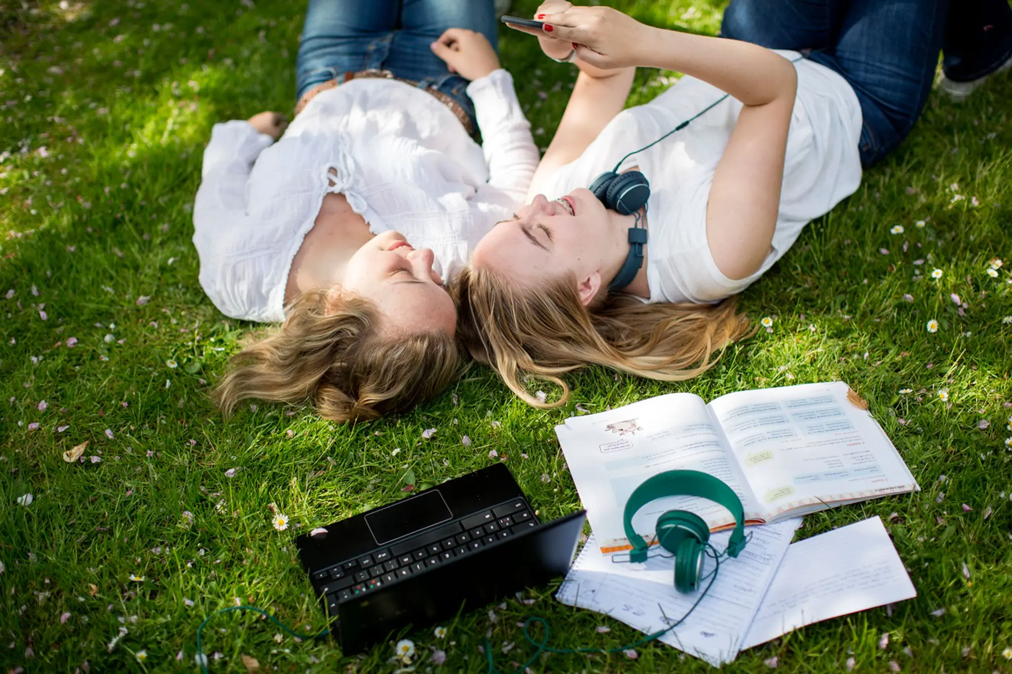 Två studenter vilar på gräsmattan, hörlurar och leenden, datorer, studentlitteratur