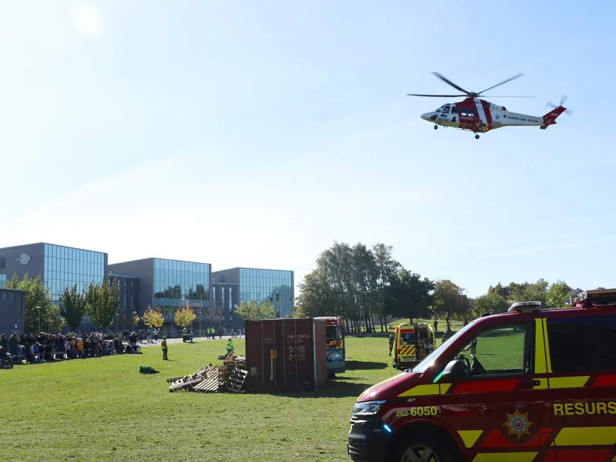 Sjöräddningshelikopter i luften och en räddningstjänstens bil i förgrunden
